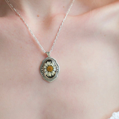 Silver necklace with a locket featuring a flower design on a person's neck.