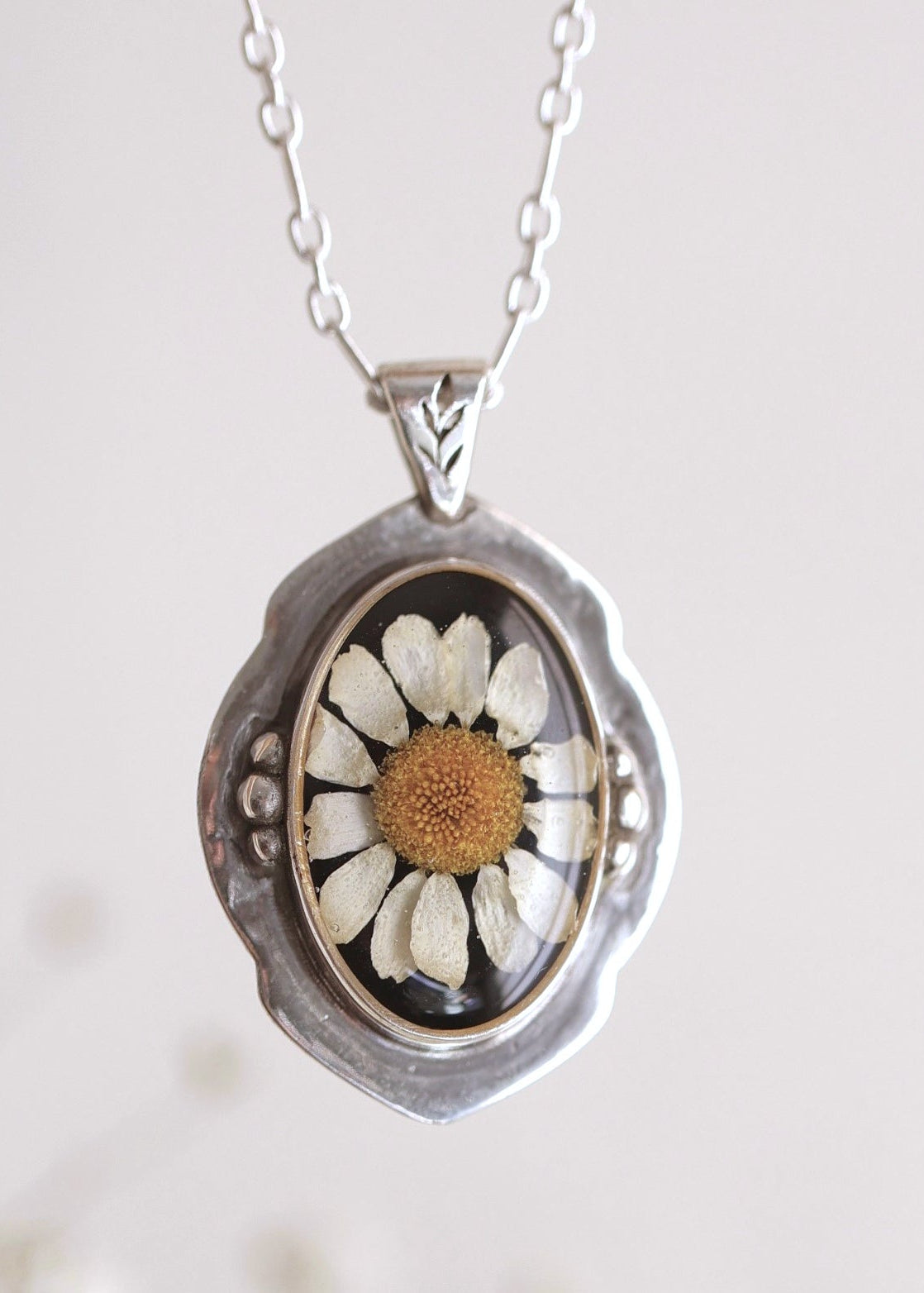 Silver necklace with a pendant featuring a pressed flower on a light background