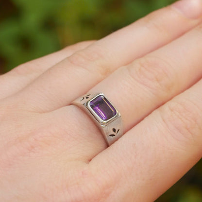 Silver ring with a purple gemstone on a hand against a blurred green background