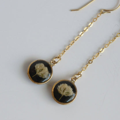 Gold earrings with black stones featuring dried flowers on a light gray background