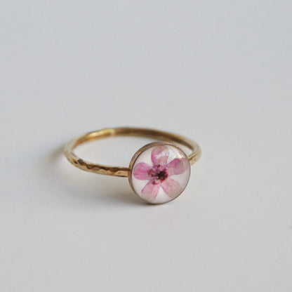 Gold ring with a pink flower in the center on a light gray background