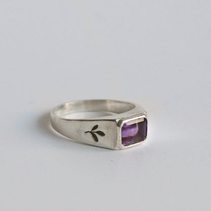 Silver ring with a purple gemstone on a light gray background