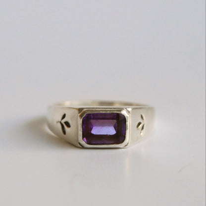 Silver ring with a purple gemstone on a light gray background