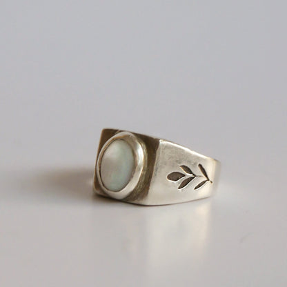 Silver ring with a circular design and leaf cutout on a light gray background