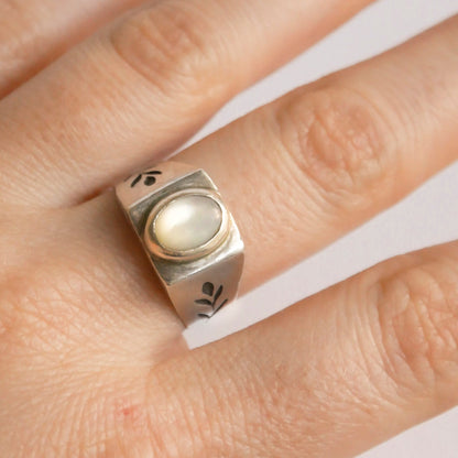 Silver ring with a central gemstone on a finger against a white background