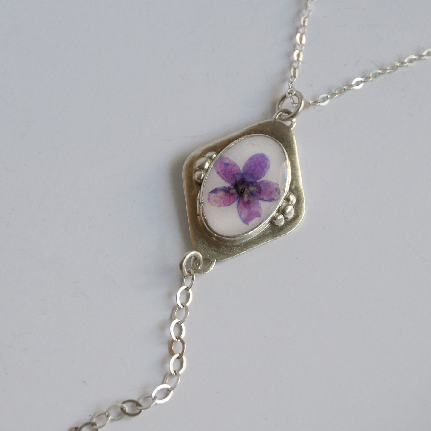 Necklace with a pendant featuring a purple flower on a white background