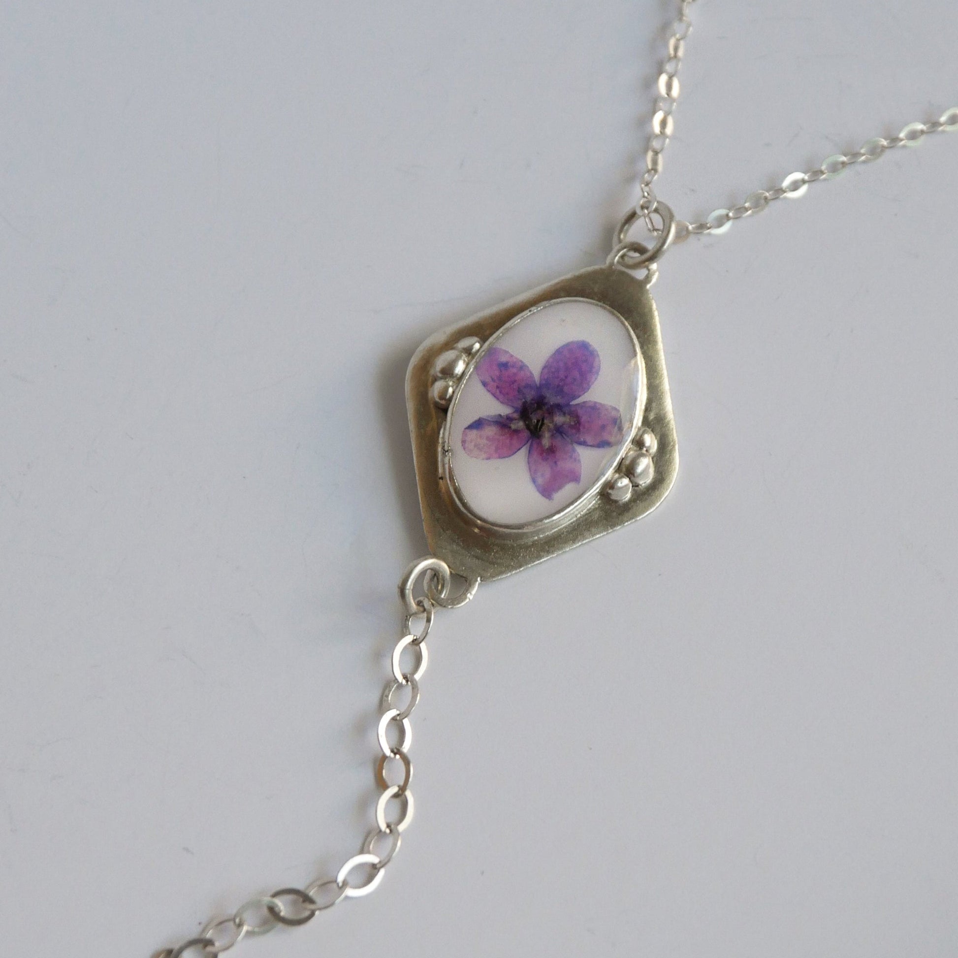 Necklace with a pendant featuring a purple flower on a white background