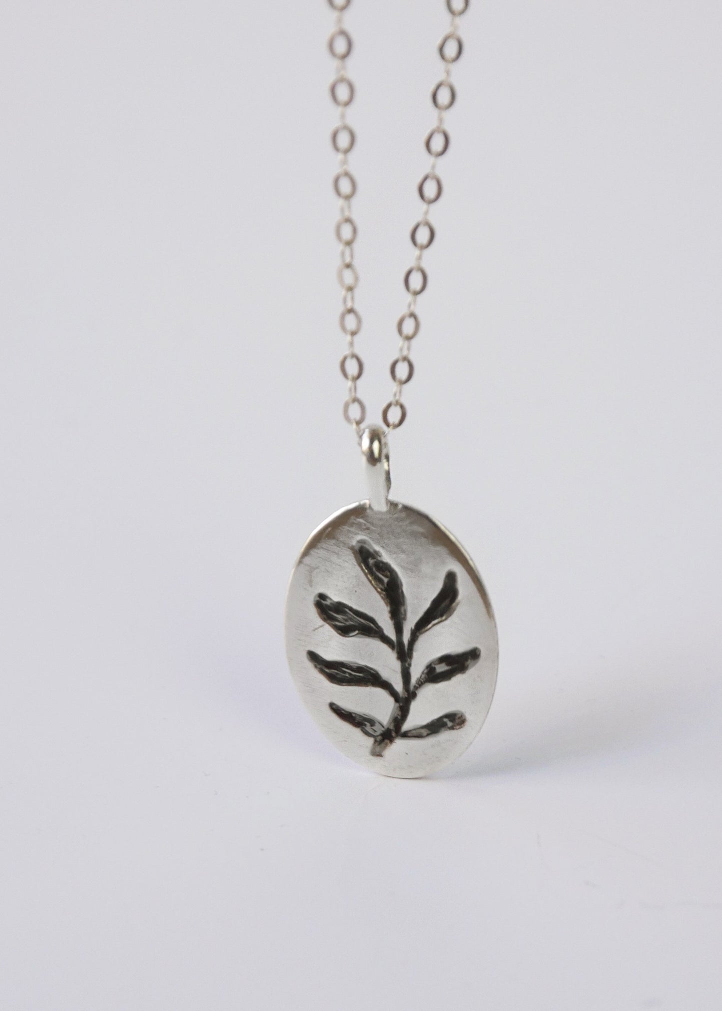Silver necklace with a leaf pendant on a white background