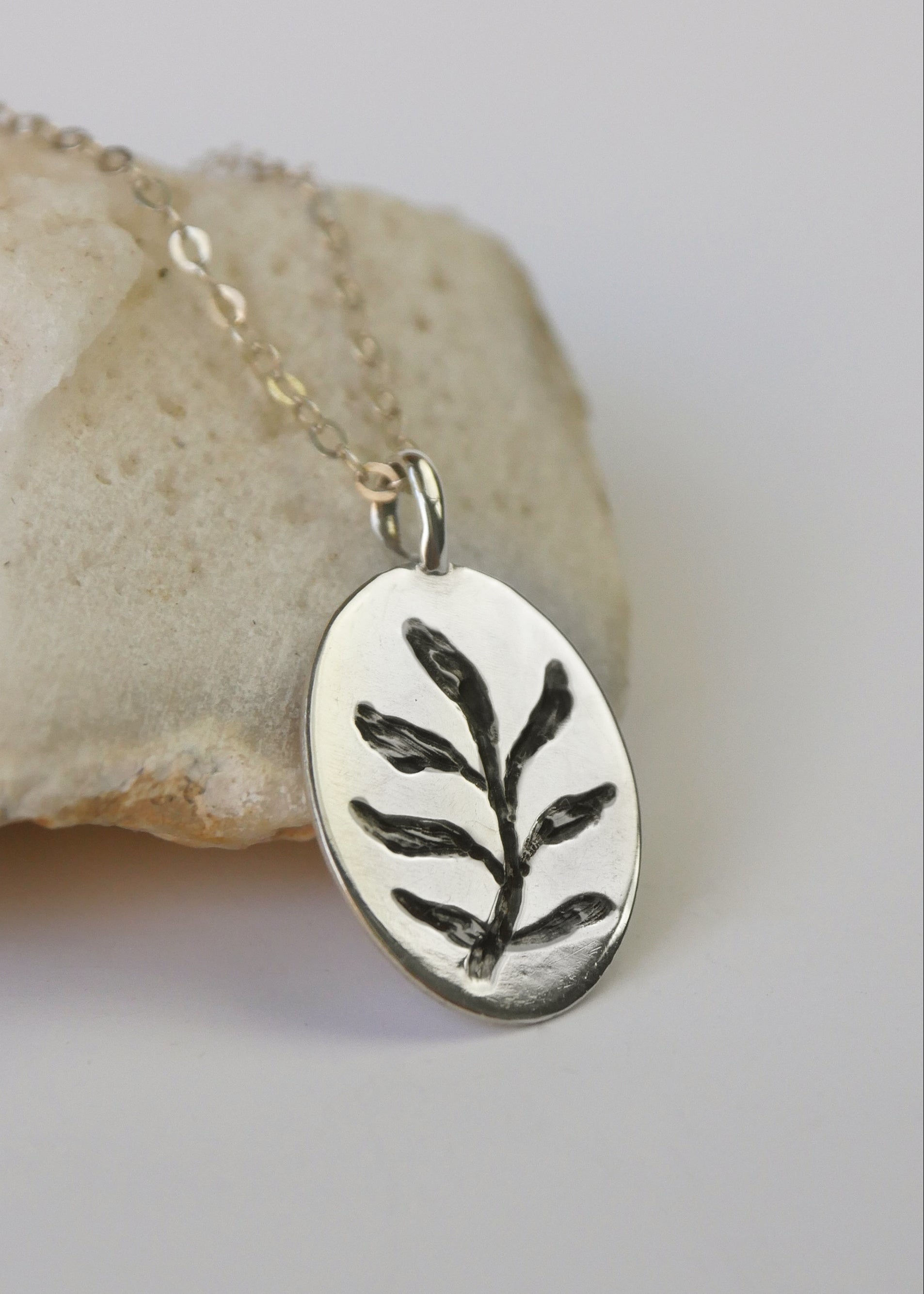 Silver pendant with leaf design on a chain, placed on a stone surface.