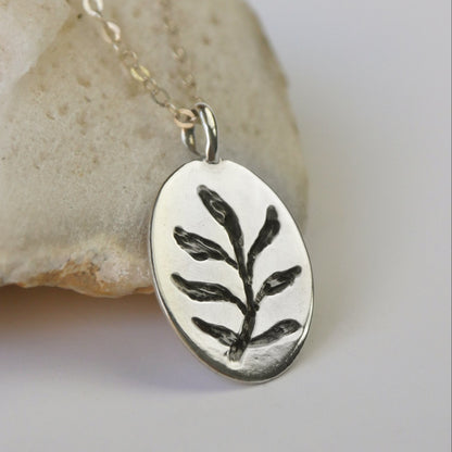 Silver pendant with leaf design on a chain, placed on a stone surface.