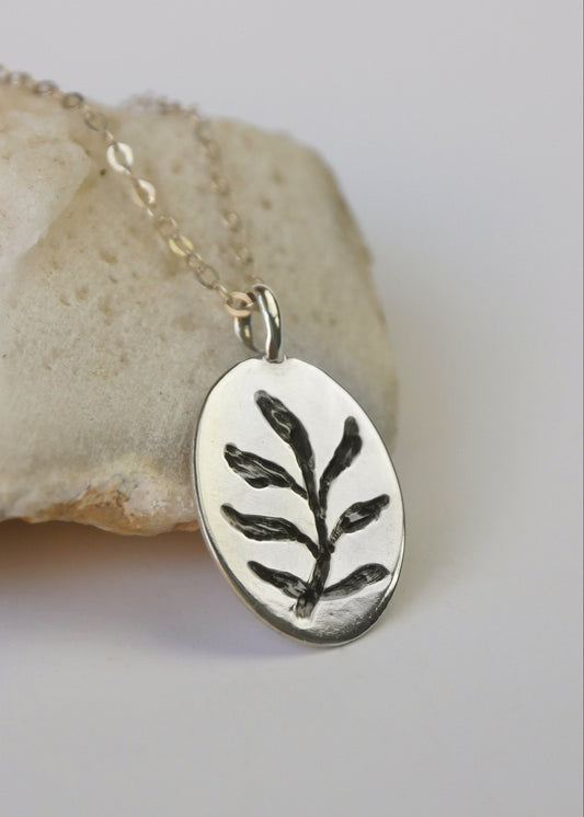 Silver pendant with leaf design on a chain, placed on a stone surface.