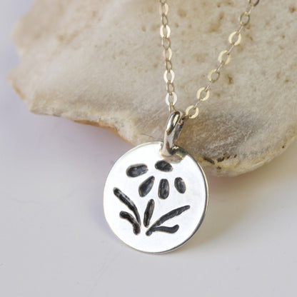 Silver necklace with a round pendant featuring a floral design, lying on a stone surface.