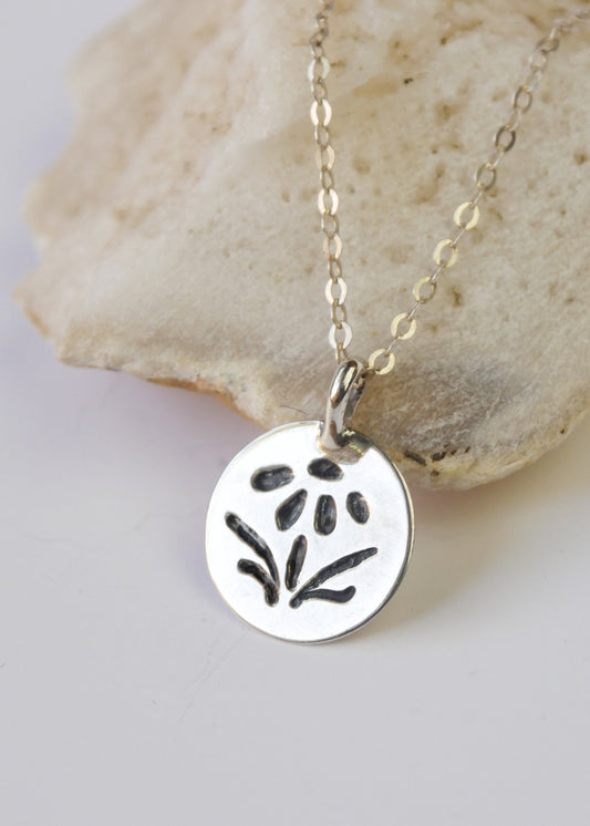 Silver necklace with a round pendant featuring a floral design, lying on a stone surface.
