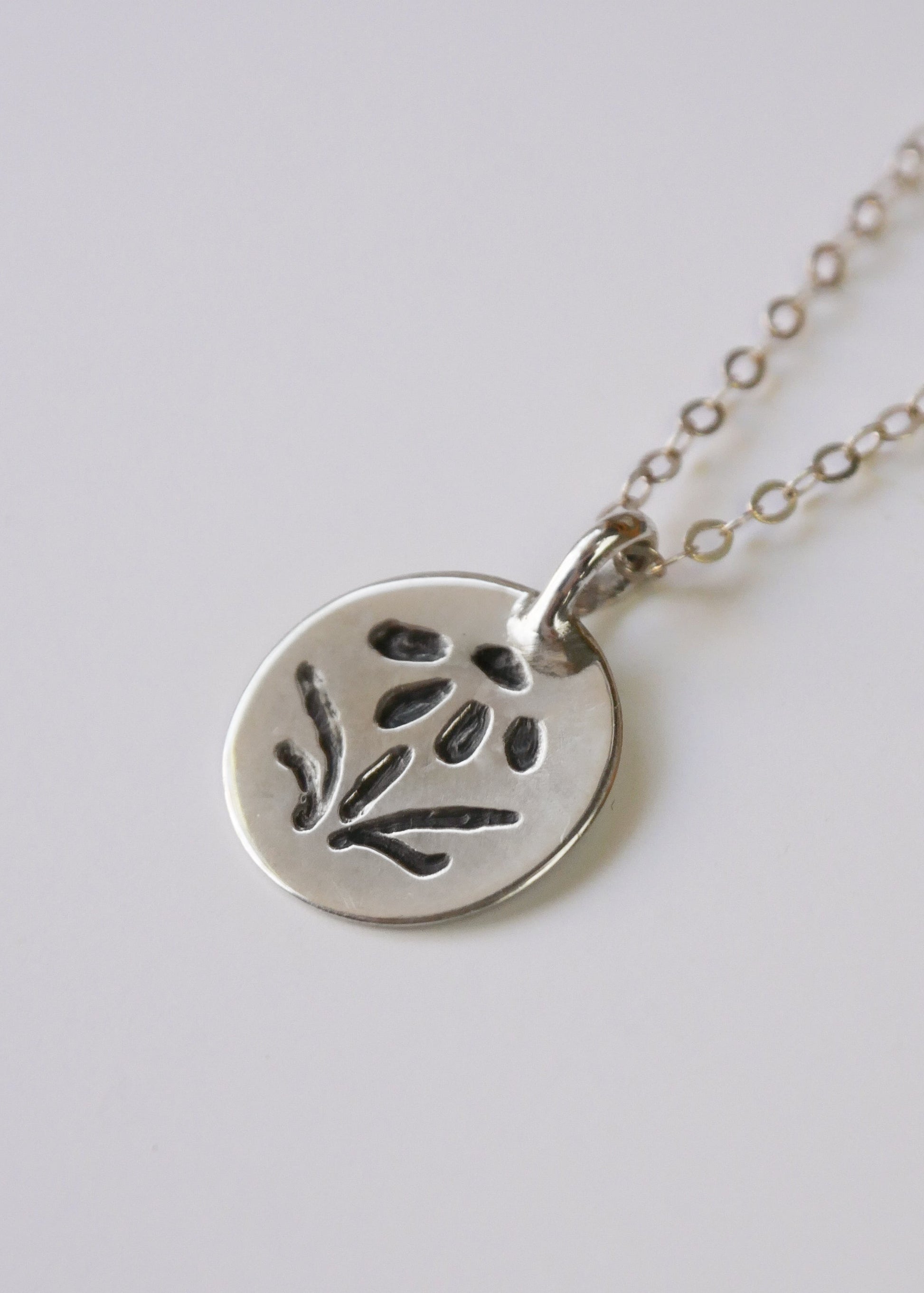 Silver necklace with a round pendant featuring an embossed design on a light gray background