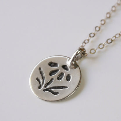 Silver necklace with a round pendant featuring an embossed design on a light gray background