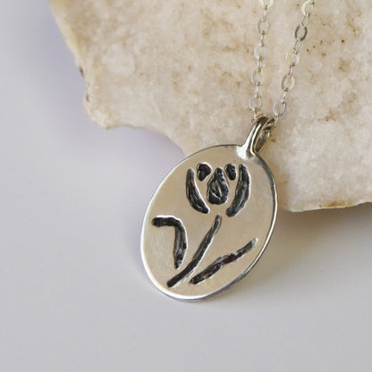 Silver pendant with floral design on a chain, placed on a stone surface.