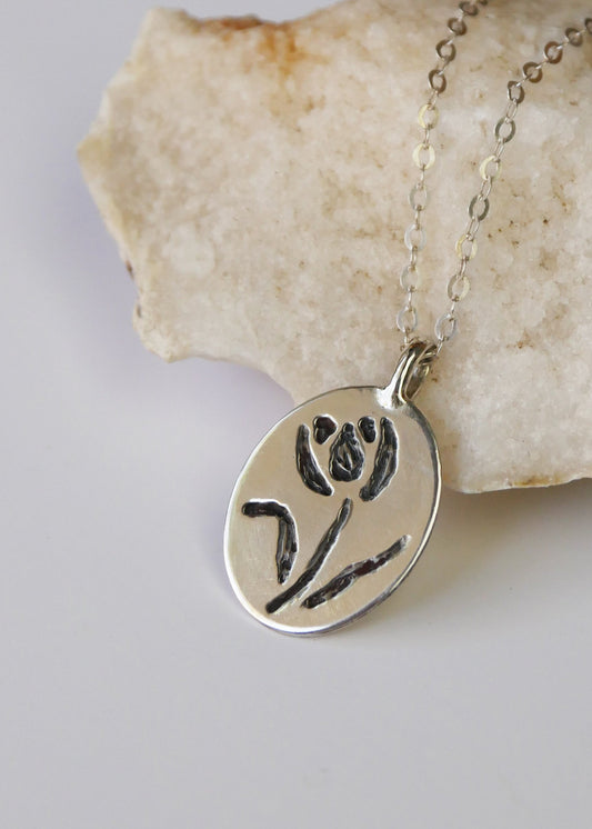 Silver pendant with floral design on a chain, placed on a stone surface.