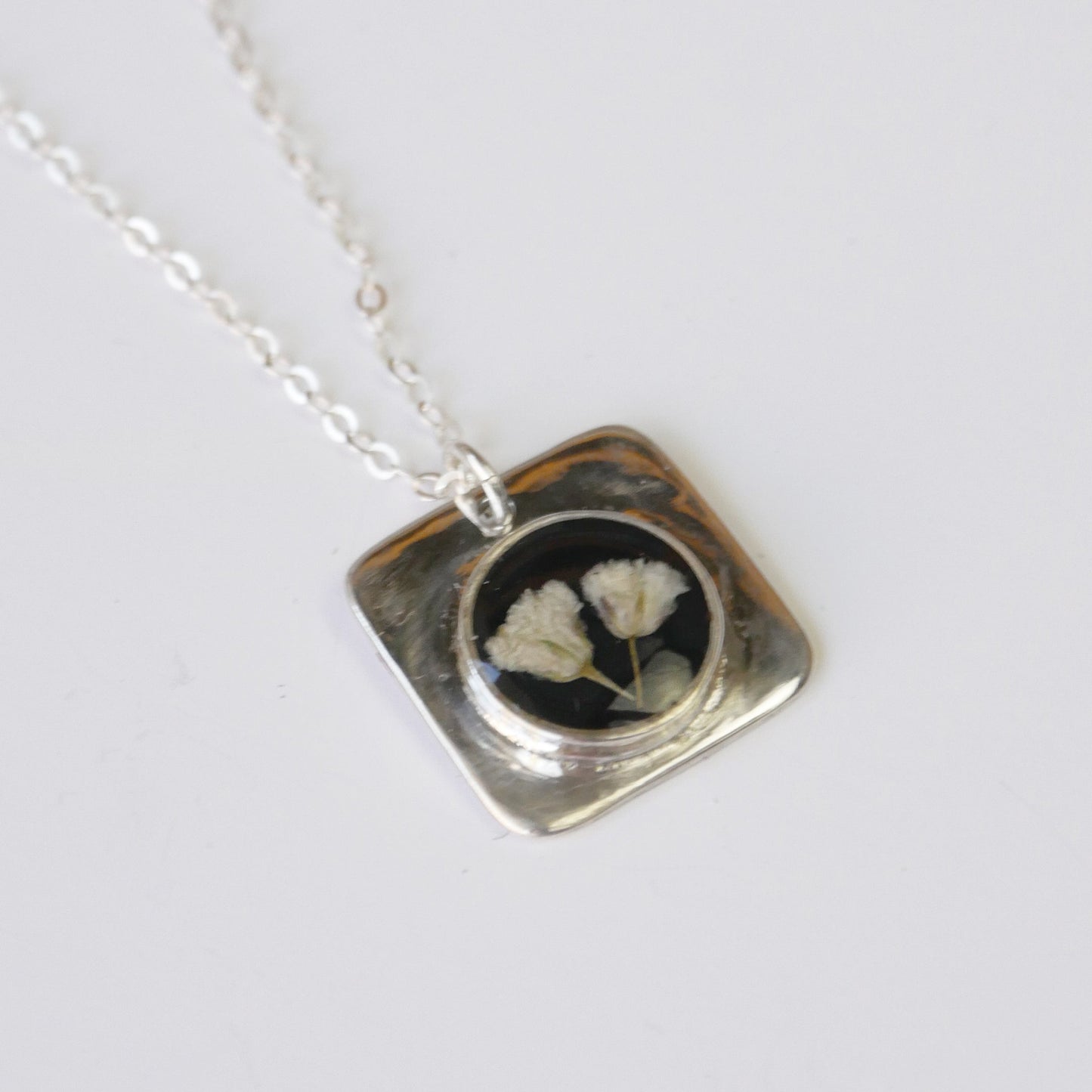 Necklace with a square pendant featuring pressed flowers on a white background