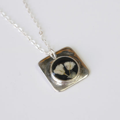 Necklace with a square pendant featuring pressed flowers on a white background