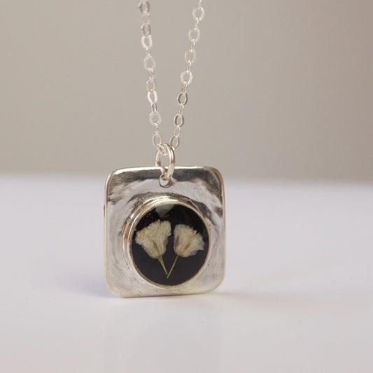 Silver necklace with a square pendant featuring a floral design on a plain background