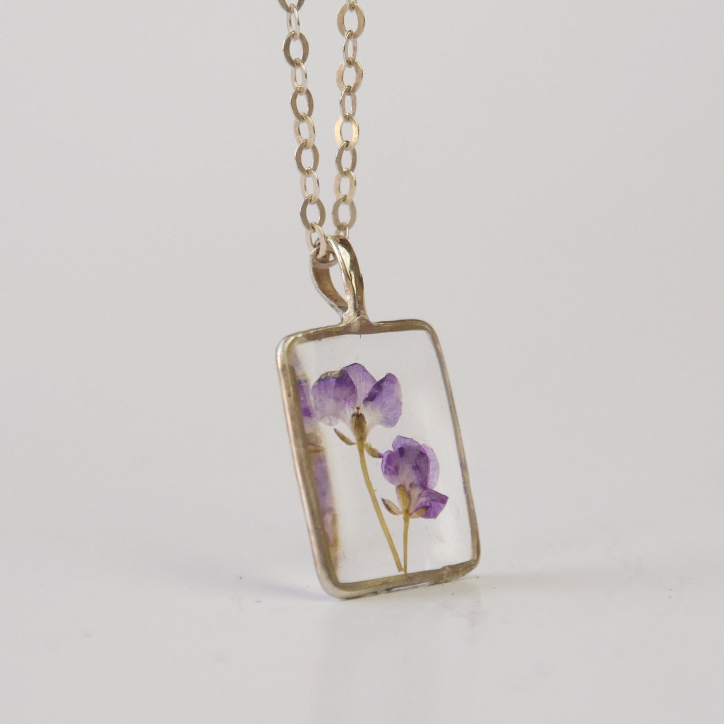 Necklace with a rectangular pendant featuring pressed flowers on a light gray background