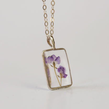Necklace with a rectangular pendant featuring pressed flowers on a light gray background