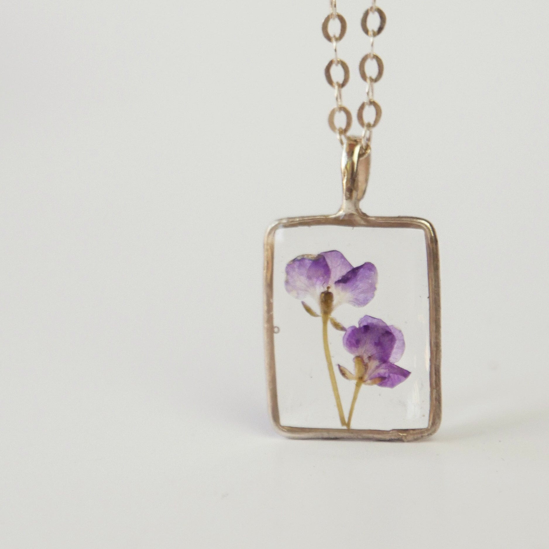Necklace with a rectangular pendant featuring pressed purple flowers on a light gray background