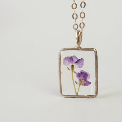 Necklace with a rectangular pendant featuring pressed purple flowers on a light gray background
