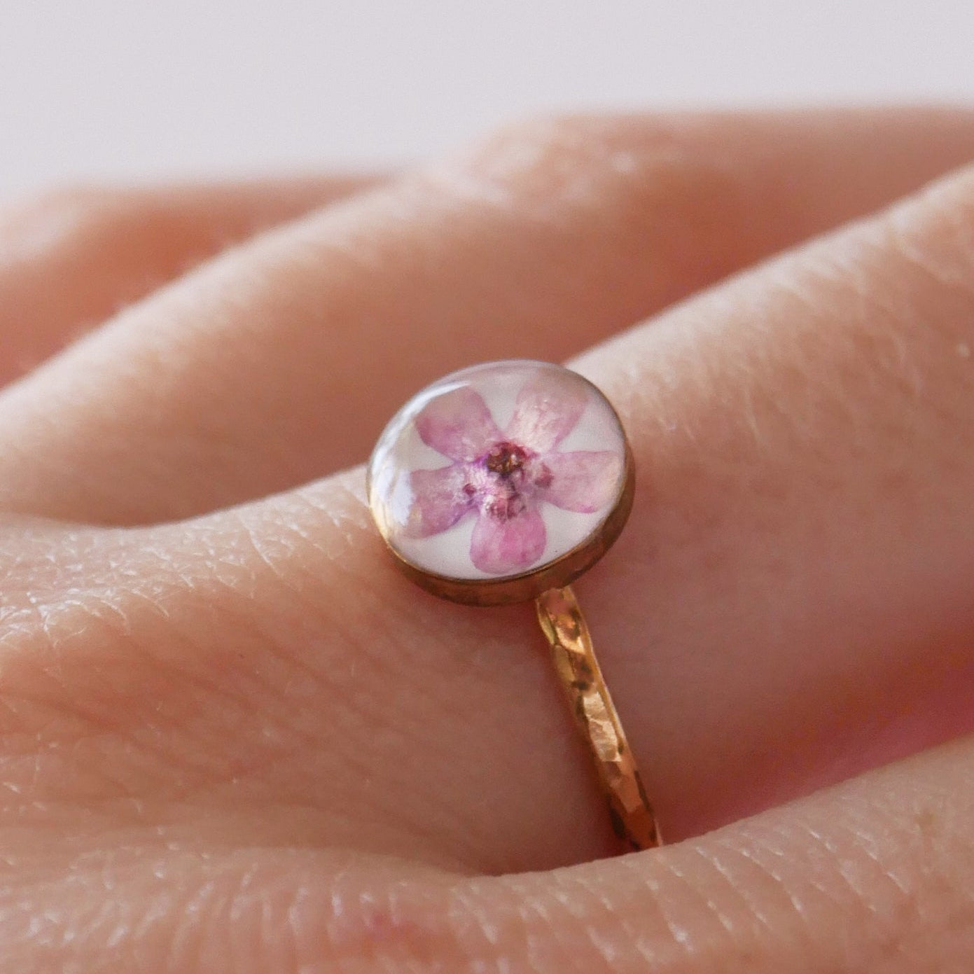 Ring with a floral design on a finger against a neutral background