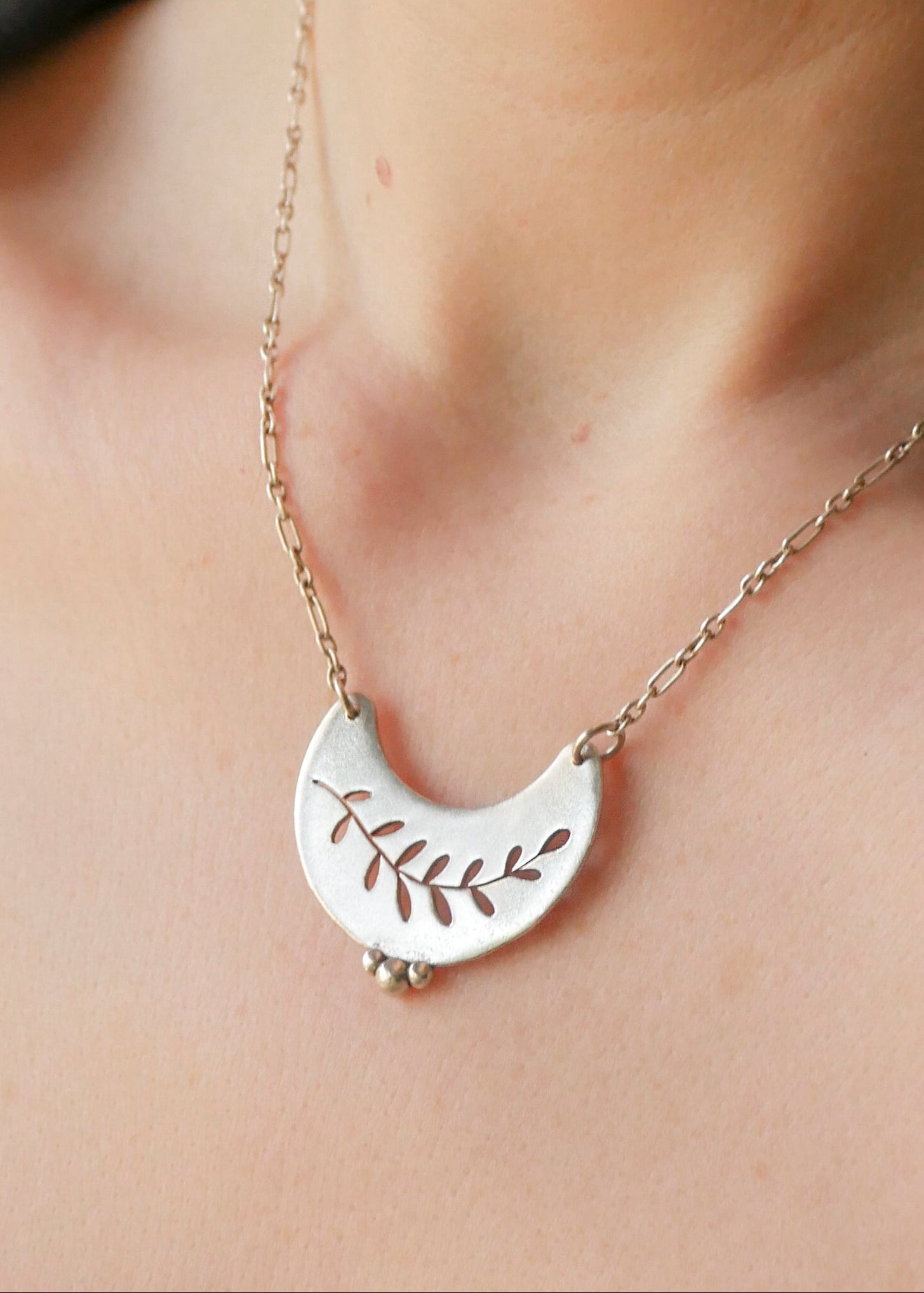 Silver necklace with a leaf design on a person's neck