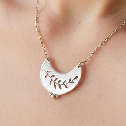 Silver necklace with a leaf design on a person's neck