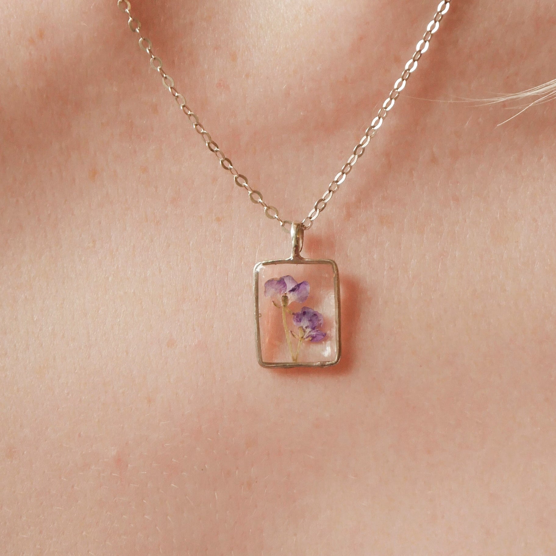 Necklace with a square pendant featuring floral design worn on a person's neck.