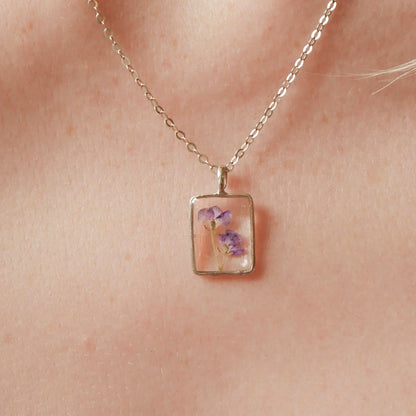 Necklace with a square pendant featuring floral design worn on a person's neck.