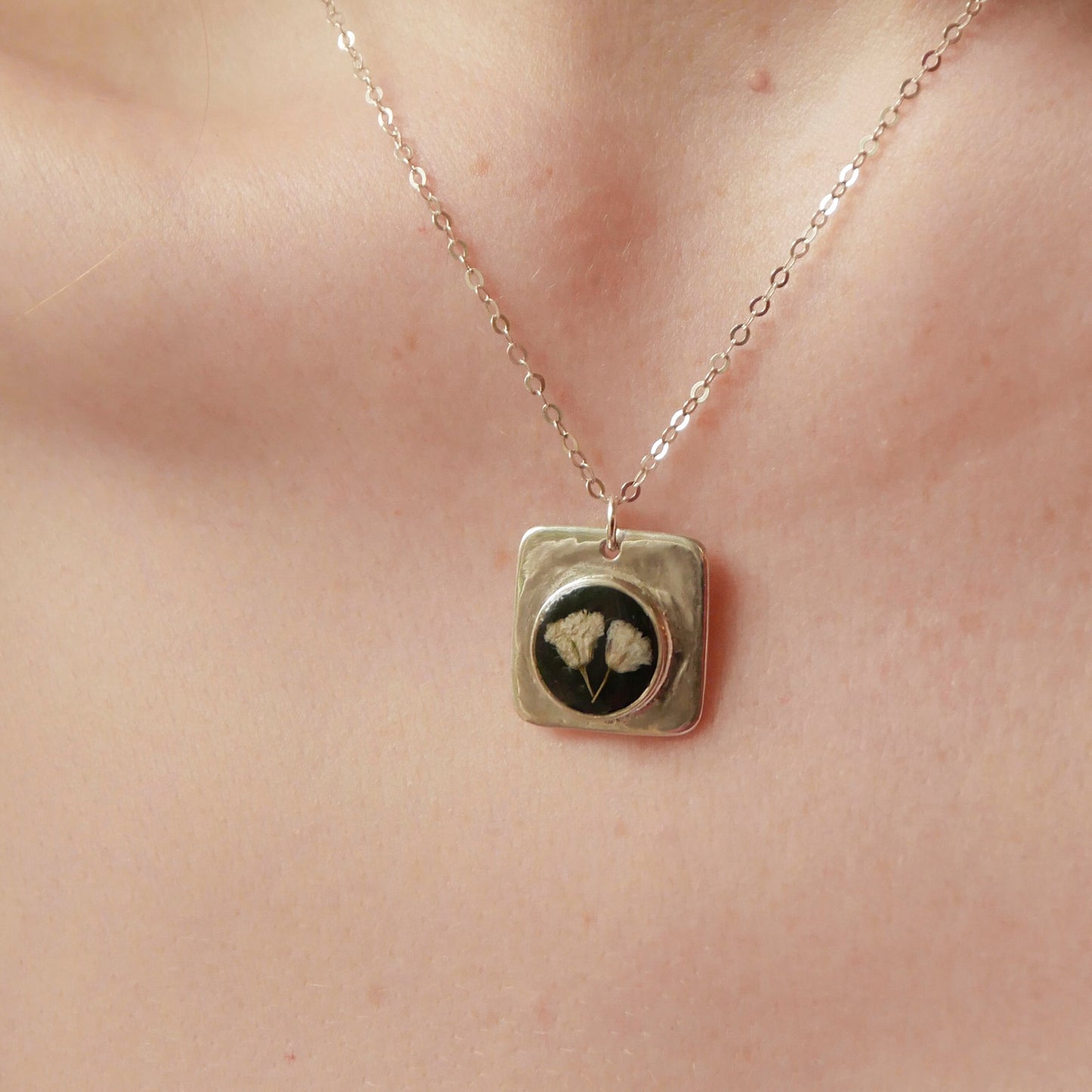 Necklace with a square pendant featuring a face design on a person's neck.