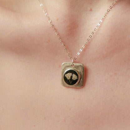 Necklace with a square pendant featuring a face design on a person's neck.