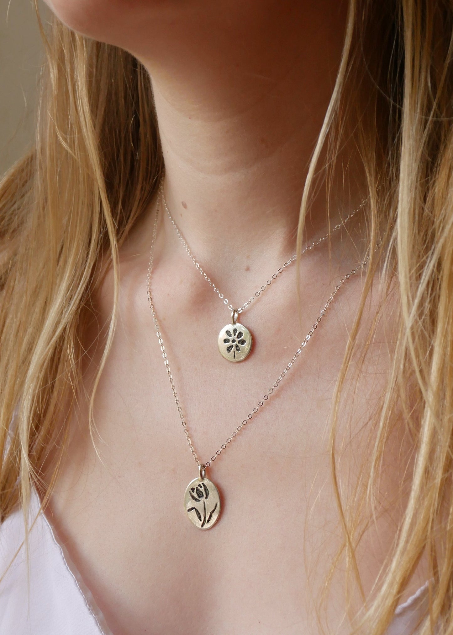 Close-up of a person wearing two delicate necklaces with floral pendants.