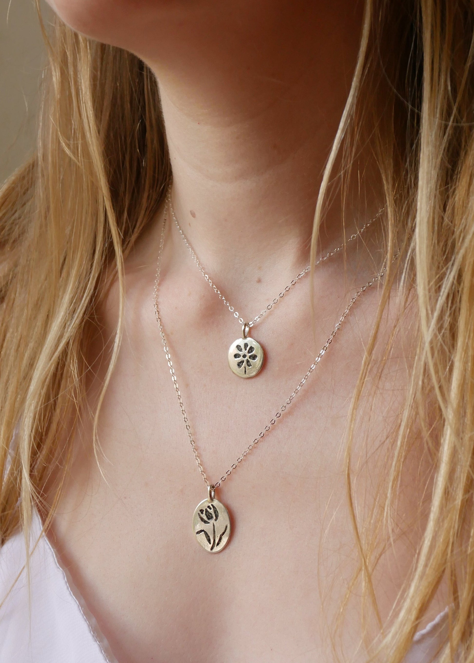 Close-up of a person wearing two delicate necklaces with floral pendants.