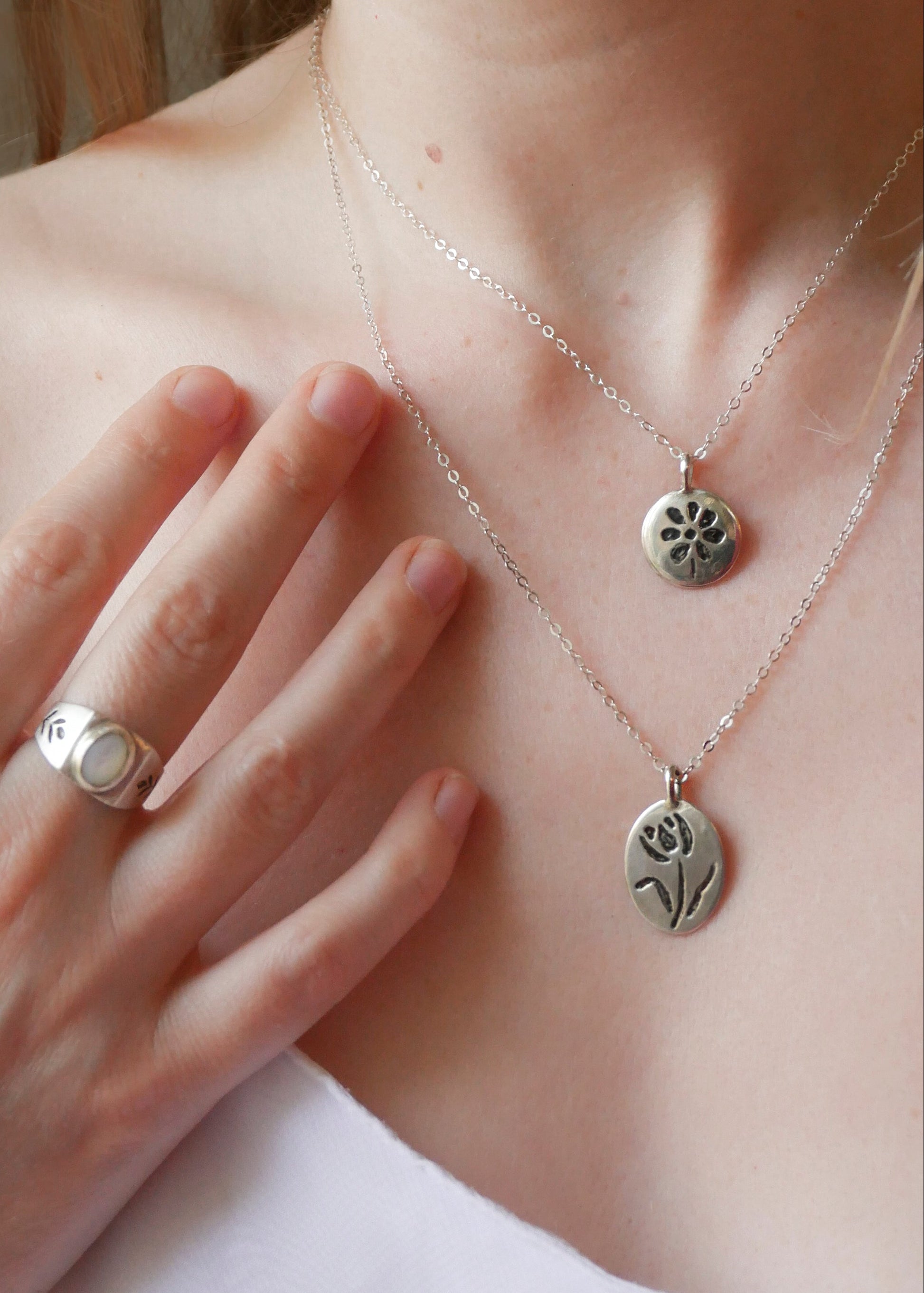 Silver necklaces with pendants on a person wearing a white top.