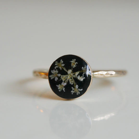 Ring with black circular stone featuring white floral design on a light gray background