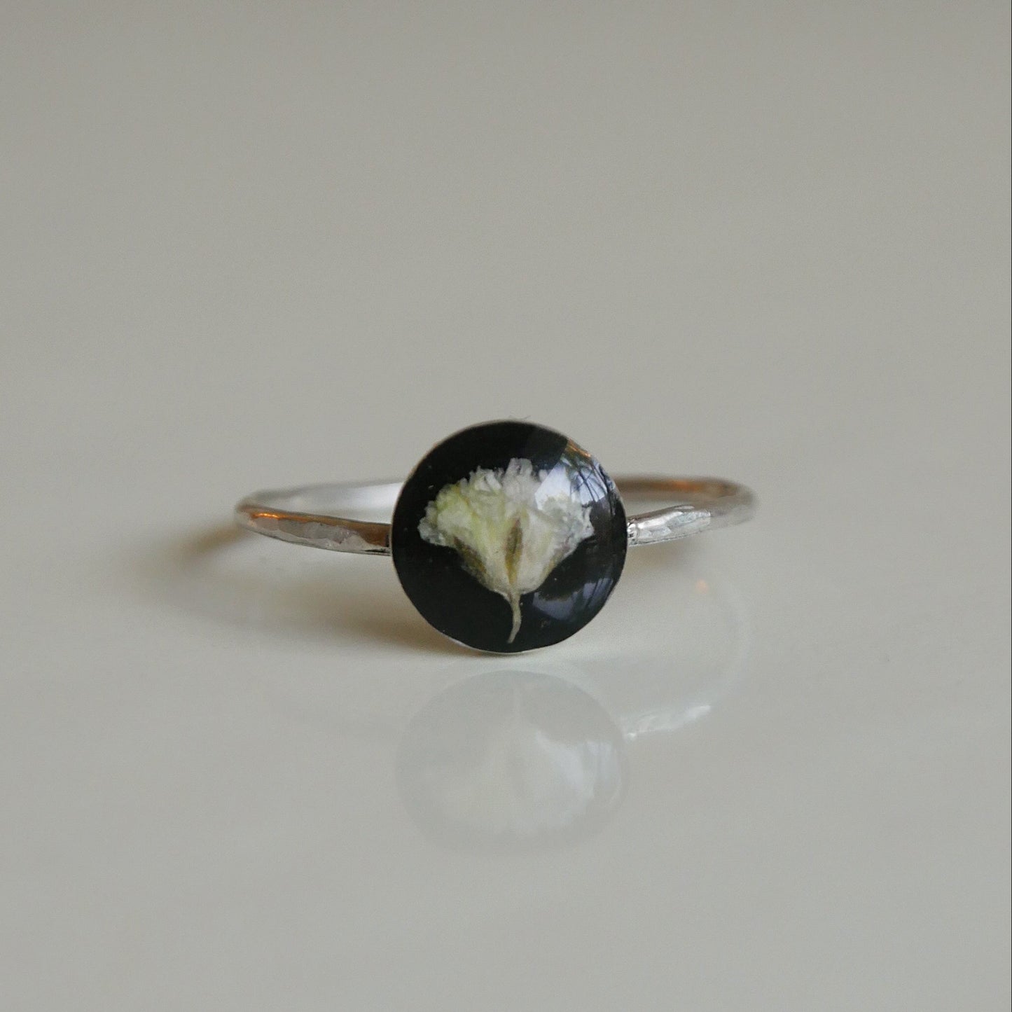 Silver ring with a black and white circular stone on a beige background