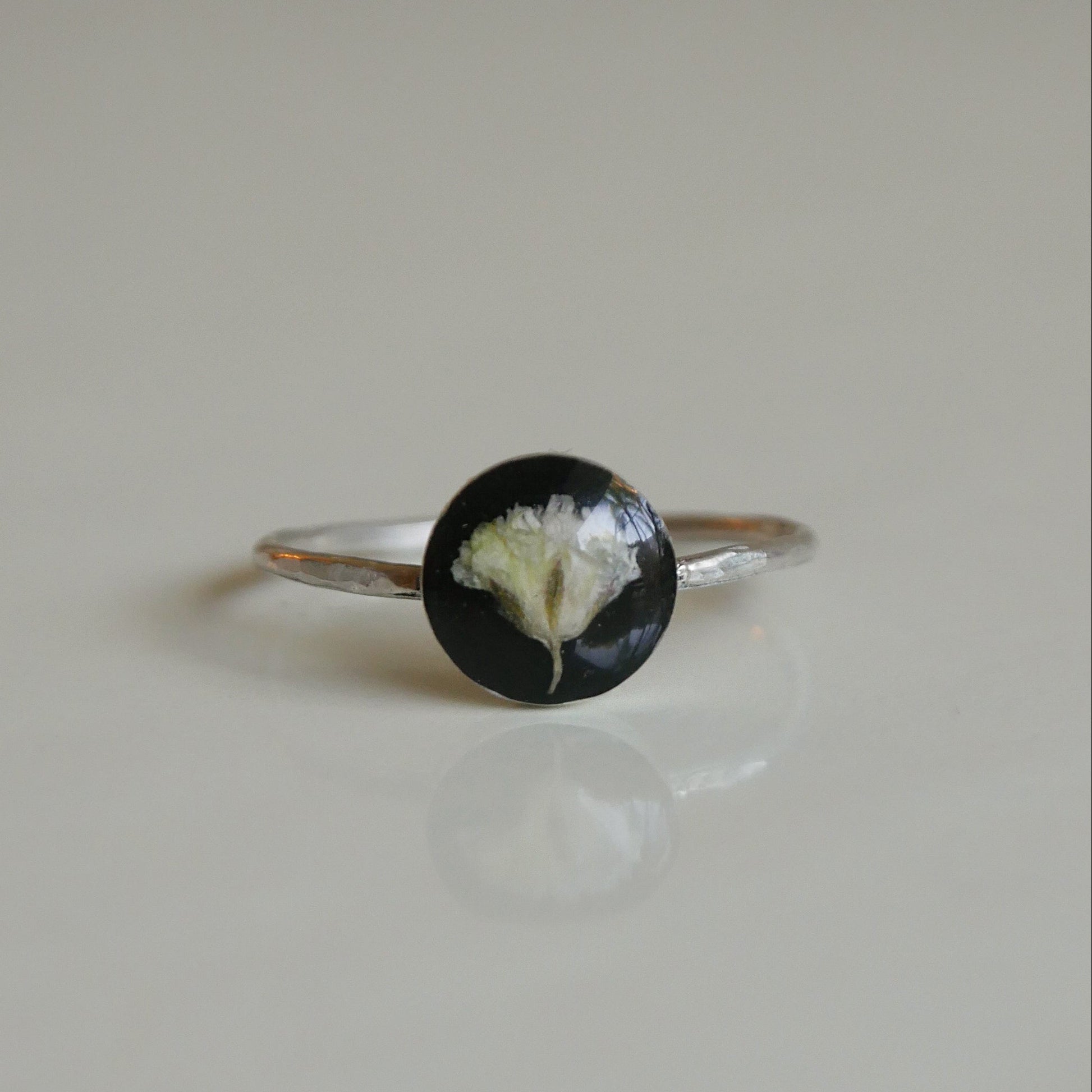 Silver ring with a black and white circular stone on a beige background
