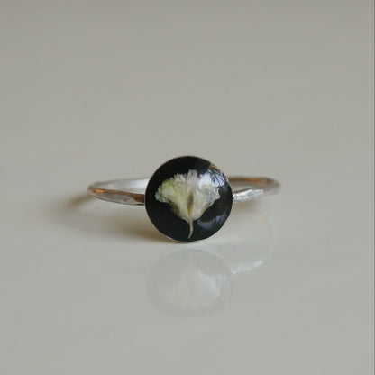 Silver ring with a black and white circular stone on a beige background
