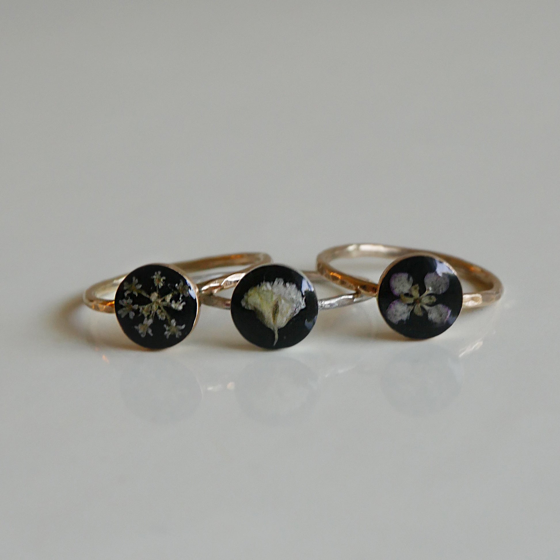 Three gold rings with black stones featuring floral designs on a light gray background