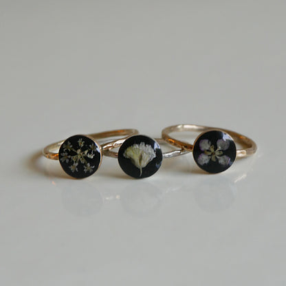 Three gold rings with black stones featuring floral designs on a light gray background