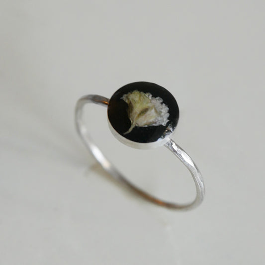 Silver ring with a black circular stone featuring a floral design on a light gray background