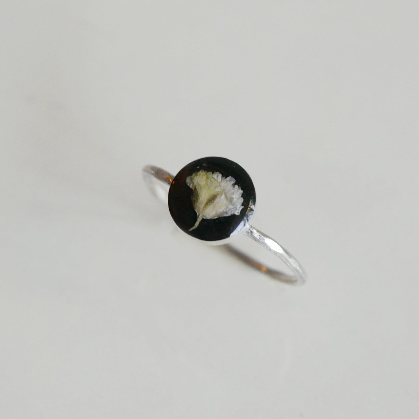 Silver ring with a black circular stone featuring a white floral design on a light gray background